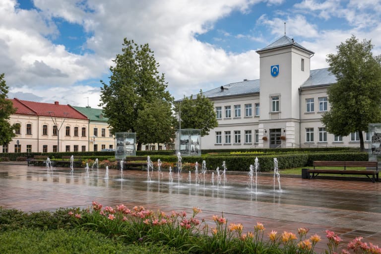 Šokantys fontanai, stiklo ekspozicijų stendai, gėlynai ir savivaldybės bokštas Utenio aikštėje Utenoje