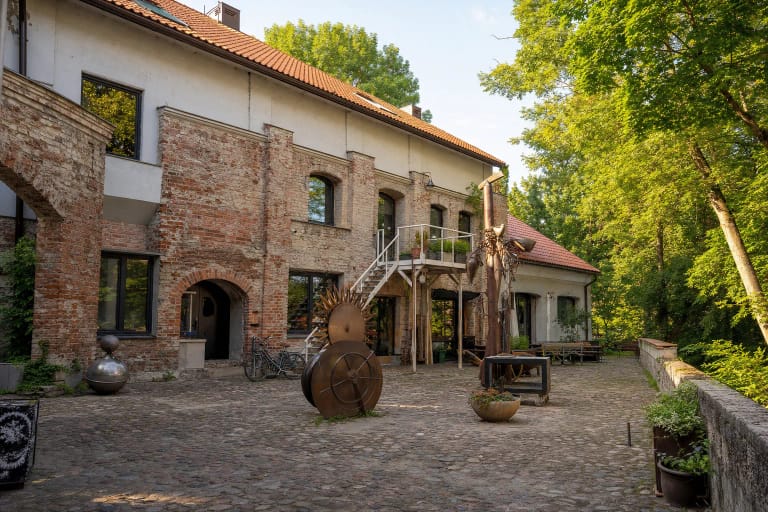 Užupio meno inkubatoriaus Galeros kiemas prie Vilnelės su mūro sienomis, baltais laiptais ir meno kūriniais