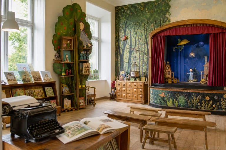 Colourful fairy-tale display with timber props, books, and a small stage inside the Children's Literature Museum