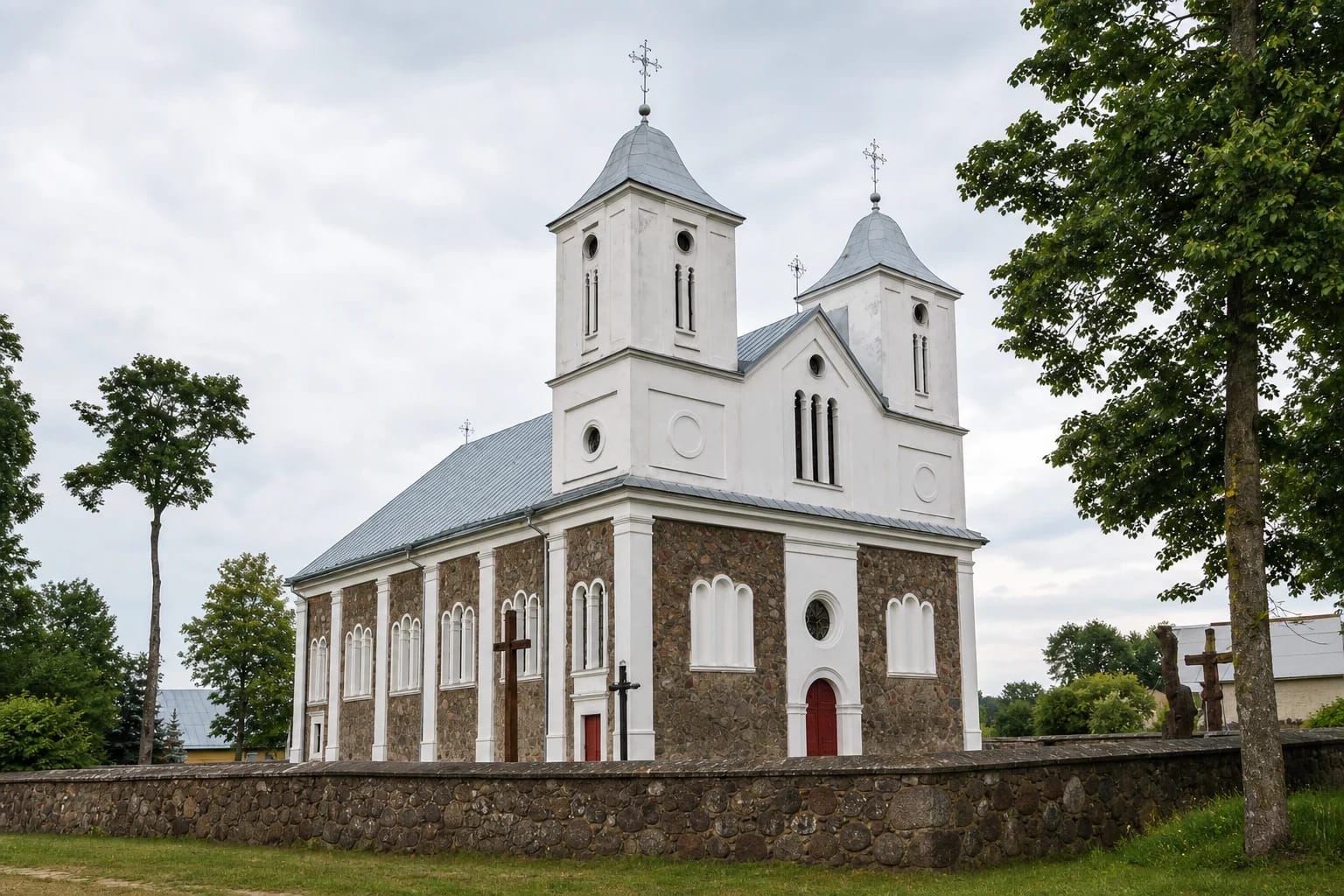 Twin towers of Vainutas Church of St John the Baptist above its fieldstone churchyard wall