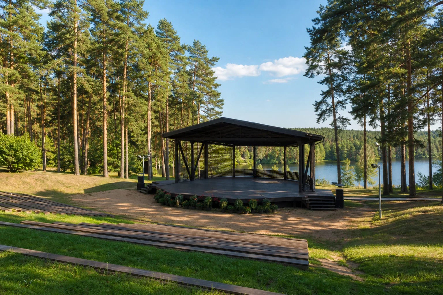 Varėnos dainų slėnio vasaros scena tarp pušų ir prie vandens esančios žiūrovų erdvės