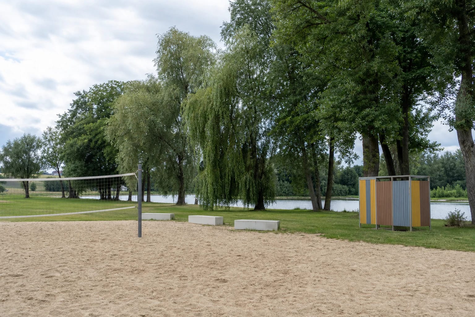 Velžys Beach sand court with a volleyball net, colourful changing cabin, and the Nevėžis shore