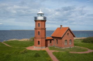 Ventė Cape red-brick lighthouse with a white lantern, red-tiled house, and the Curonian Lagoon