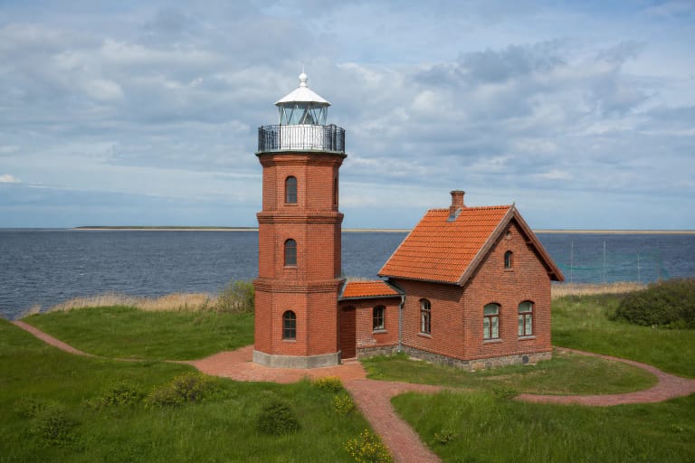 Ventė Cape red-brick lighthouse with a white lantern, red-tiled house, and the Curonian Lagoon