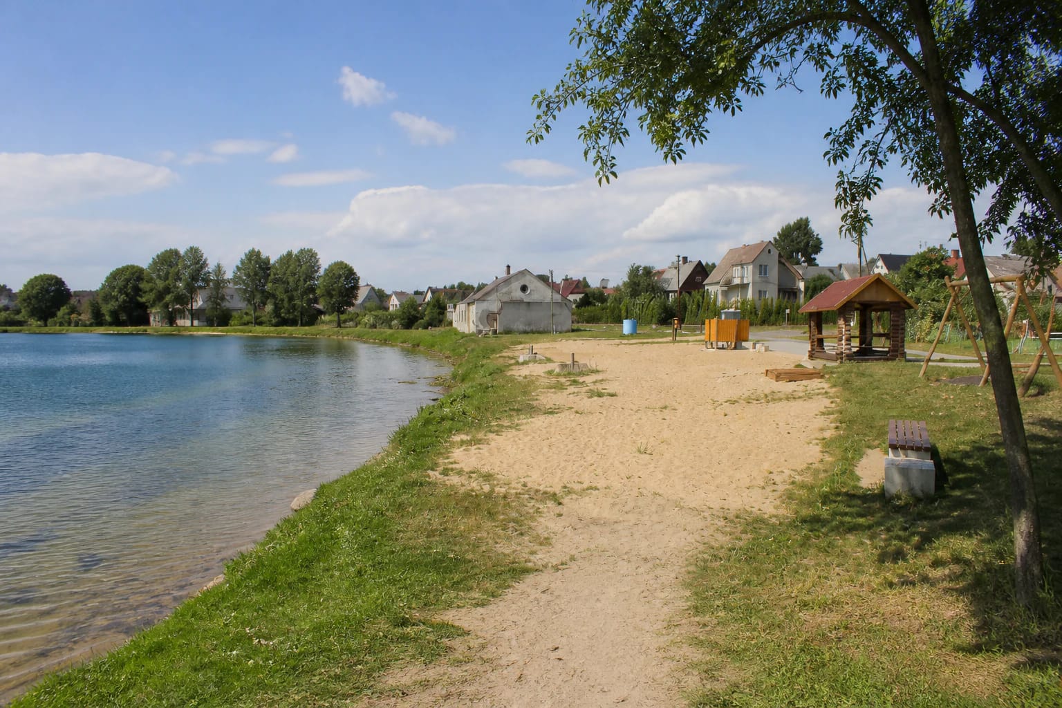 Small Vievio Beach beside calm lake water with a sandy shore, trees and a simple shelter
