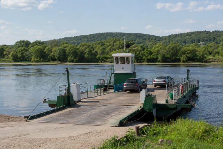 The green-and-white Vilkynė motor ferry carrying two passenger cars at the Vilkija ramp between wooded banks of the Nemunas