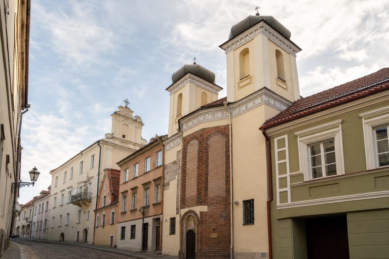 Vilniaus Dievo Gailestingumo šventovės raudonų plytų fasadas ir du šviesūs bokštai siauroje Dominikonų gatvėje