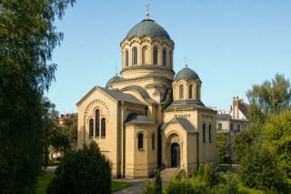 Жёлтая кирпичная Вильнюсская церковь иконы Божией Матери «Знамение» с тёмным центральным куполом, малыми куполами и золотыми крестами среди деревьев Жверинаса