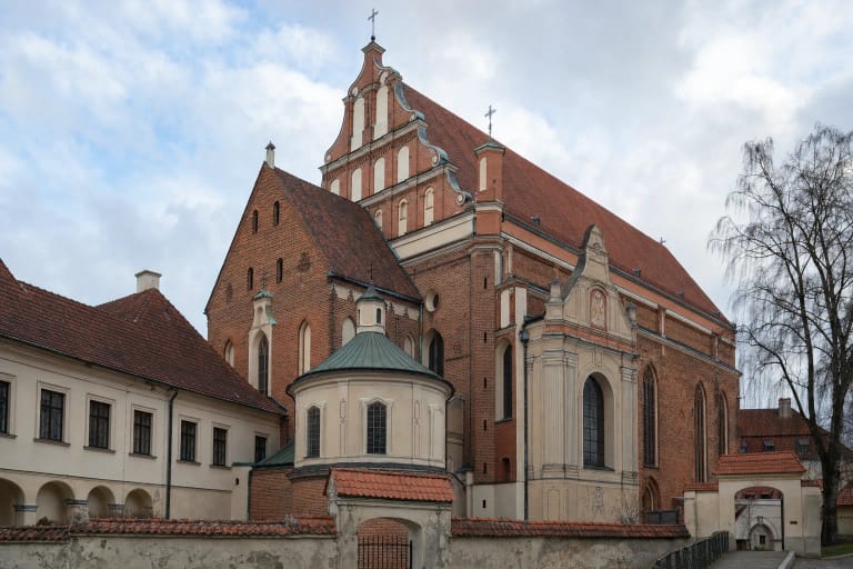Pale Baroque facade and red-tiled roof of the Franciscan Church in a Vilnius Old Town courtyard