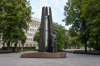 Bronze figure and tall stylised bell tower of the Vincas Kudirka monument in a tree-lined Vilnius square
