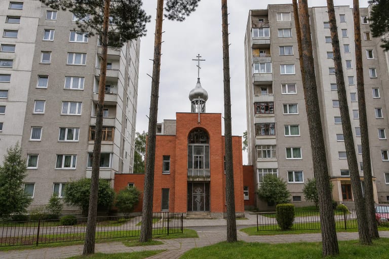 Raudonų plytų Visagino Jono Krikštytojo gimimo cerkvė su sidabriniu kupolu tarp pilkų daugiabučių ir pušų