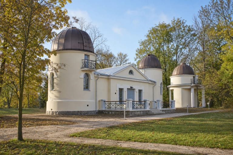 Šviesus VU Idėjų observatorijos kompleksas Vilniuje su trimis tamsiais sukamais kupolais tarp medžių