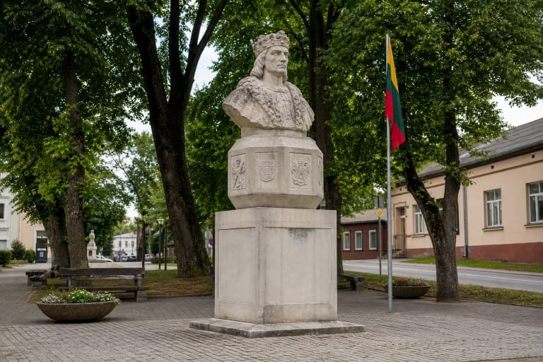 Светлый бюст Витовта Великого на двухчастном постаменте среди деревьев на площади Юрбаркаса