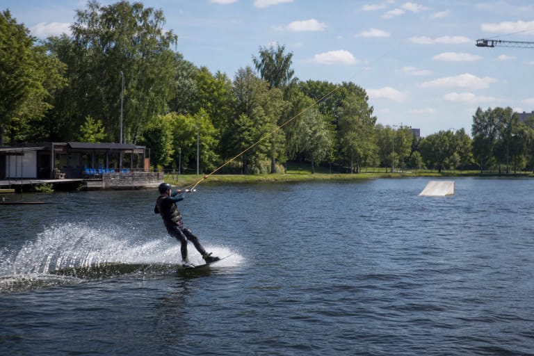 A cable wakeboarder crossing the Ekranas reservoir beside the green urban shore of Panevėžys