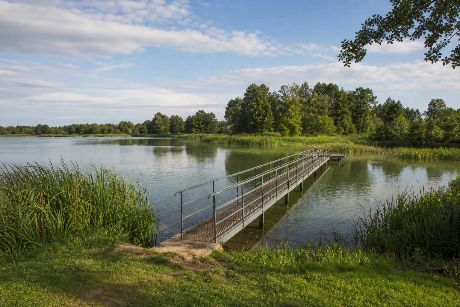 Quiet Lake Ygla shore with a narrow metal bridge, reeds, and a wooded far bank