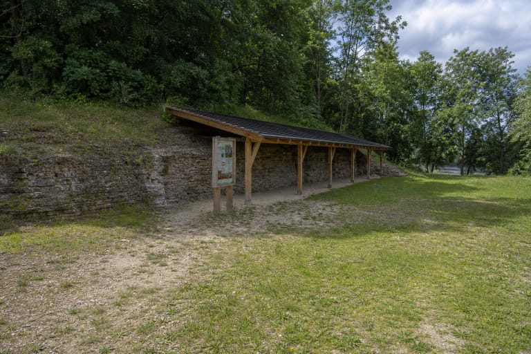 Low yellow-grey dolomite wall of Žagarė Outcrop beneath a simple timber shelter beside the grassy floor of the former quarry