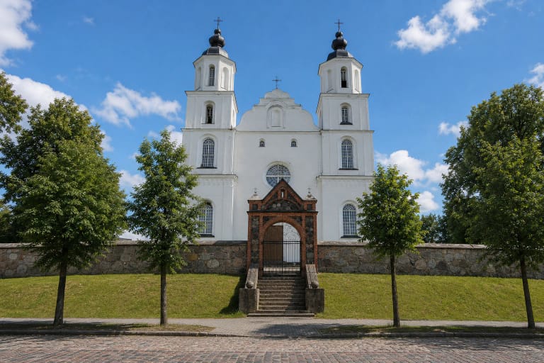 White-plastered Zarasai church with two Baroque towers, a wavy pediment, mature trees, and a town street
