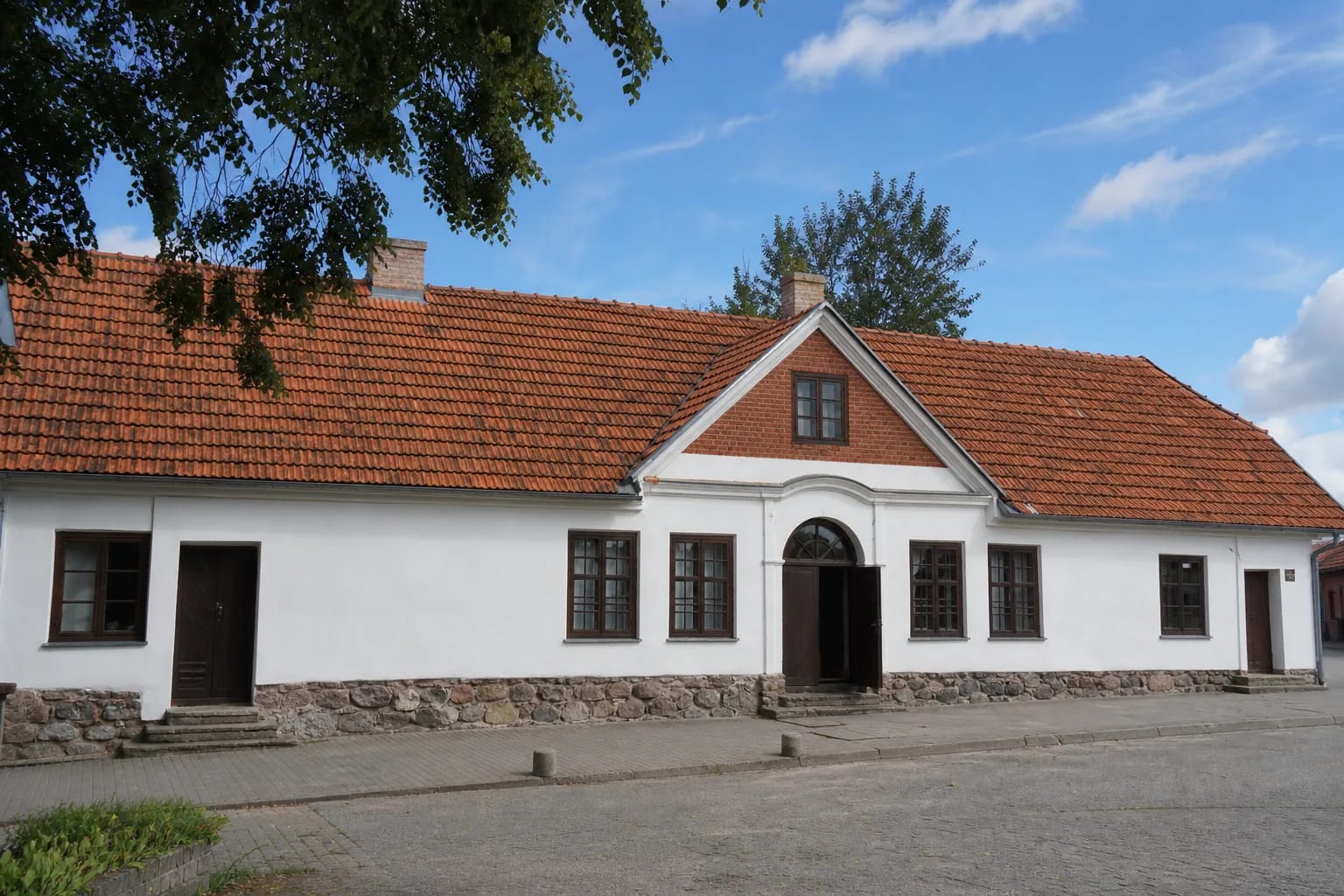 Baltas Žeimelio muziejaus Žiemgala pastatas su raudonų čerpių stogu prie miestelio gatvės