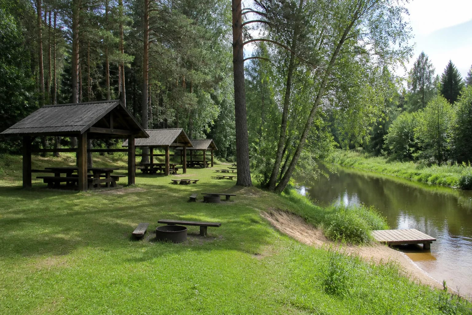Žeimena Campsite picnic shelters among pines beside the river and a wooden landing
