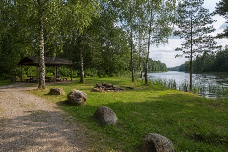 A Žingiai Campsite shelter, fire site, boulders, and water at the Asveja channel