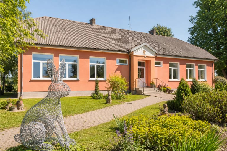 Salmon-coloured Rabbit Museum building in Sasnava with a large wire rabbit sculpture and a tended garden