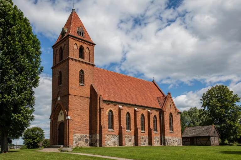 Žukų evangelikų liuteronų raudonų plytų bažnyčia su aukštu bokštu ir akmens cokoliu