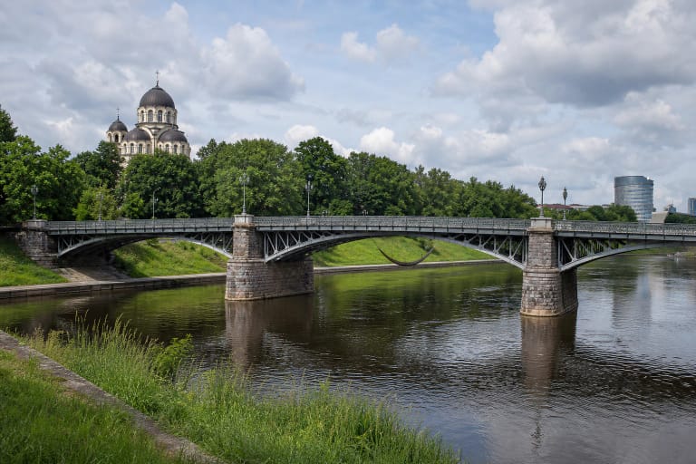 Žvėryno tiltas per Nerį su trimis plieninių santvarų tarpatramiais, akmens atramomis ir cerkvės kupolais už medžių